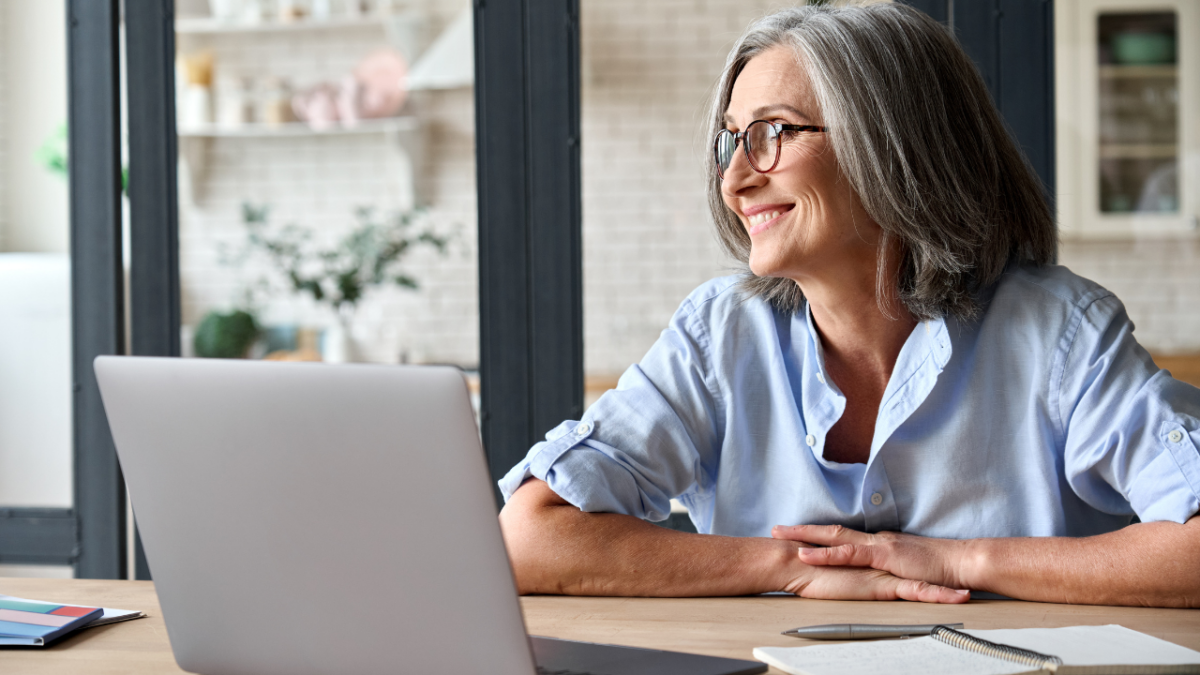 older woman sitting at home with a computer smiling