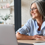 older woman sitting at home with a computer smiling