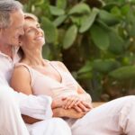 middle-aged couple sitting outdoors cuddling by pool