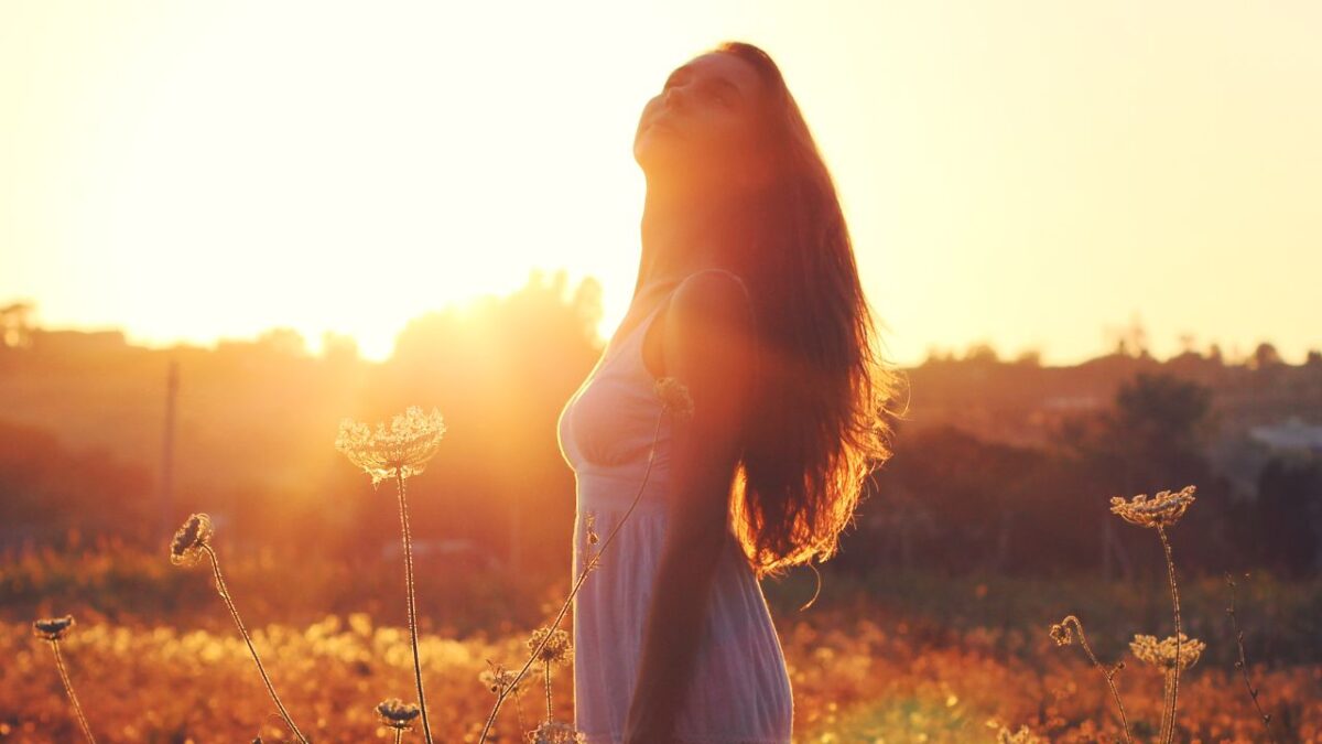 A woman standing in a sunlit field with eyes closed, symbolizing peace and clarity during hormonal changes
