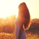 A woman standing in a sunlit field with eyes closed, symbolizing peace and clarity during hormonal changes