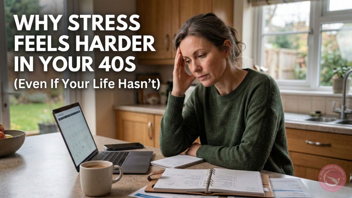 A concerned woman in her 40s sits at a kitchen counter with her hand to her head, looking at a laptop and planner.