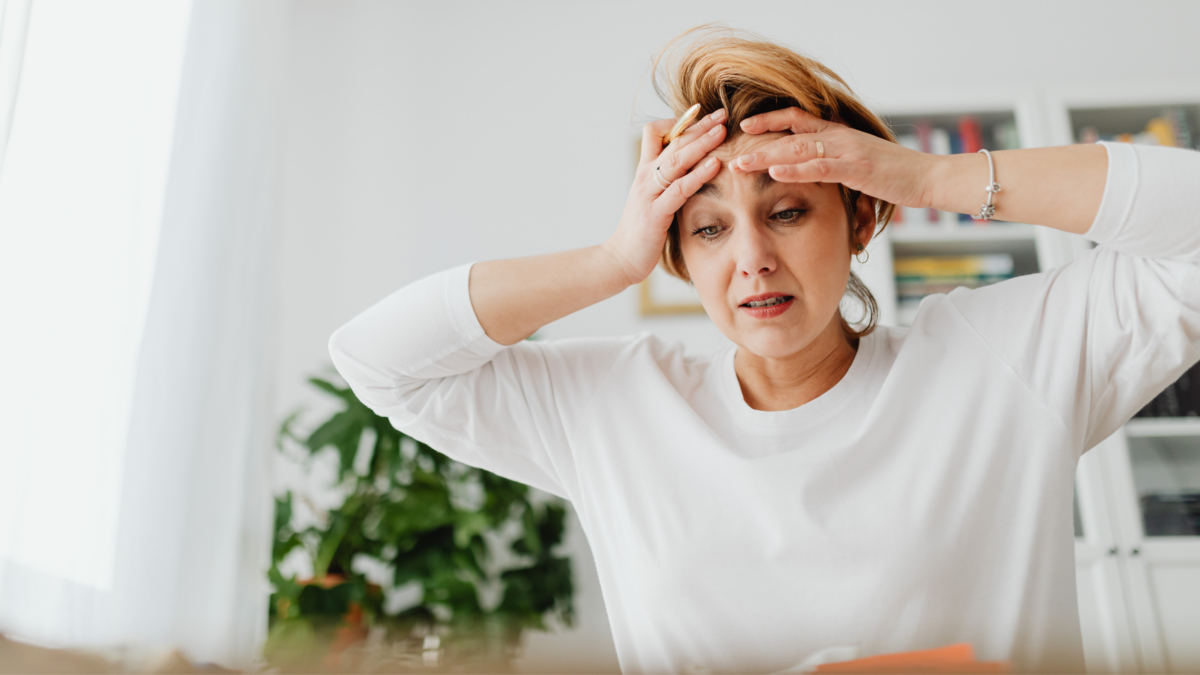 Woman in perimenopause looking emotionally overwhelmed and stressed while holding her head indoors.