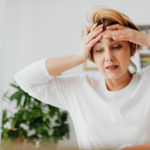 Woman in perimenopause looking emotionally overwhelmed and stressed while holding her head indoors.