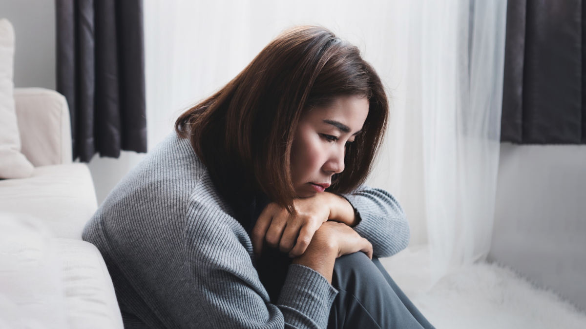Woman sitting alone looking emotionally overwhelmed and exhausted during early perimenopause symptoms related to stress, anxiety, and hormonal changes.
