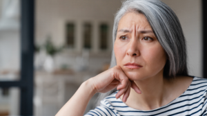 Thoughtful midlife woman sitting at home looking emotionally overwhelmed during menopause and self-care burnout