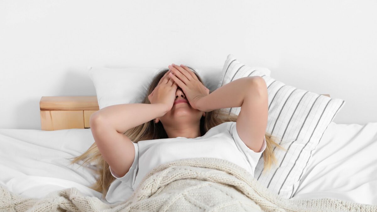 Woman lying in bed covering her face after waking up exhausted despite a full night’s sleep, illustrating menopause-related fatigue and poor sleep quality.