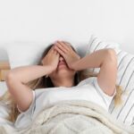 Woman lying in bed covering her face after waking up exhausted despite a full night’s sleep, illustrating menopause-related fatigue and poor sleep quality.
