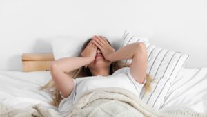 Woman lying in bed covering her face after waking up exhausted despite a full night’s sleep, illustrating menopause-related fatigue and poor sleep quality.