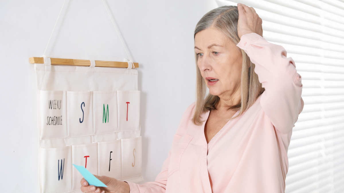 Woman experiencing menopause brain fog while looking at a note beside a weekly schedule.