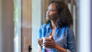 Woman holding a mug of coffee while looking out a window, illustrating the question of whether coffee affects hot flashes during menopause.