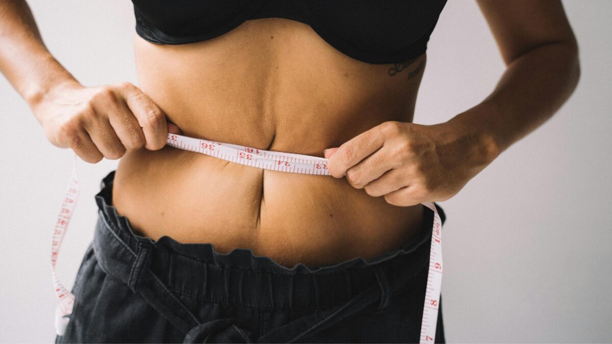 Woman measuring her waist with a tape measure, illustrating menopause metabolism and changes in abdominal fat.